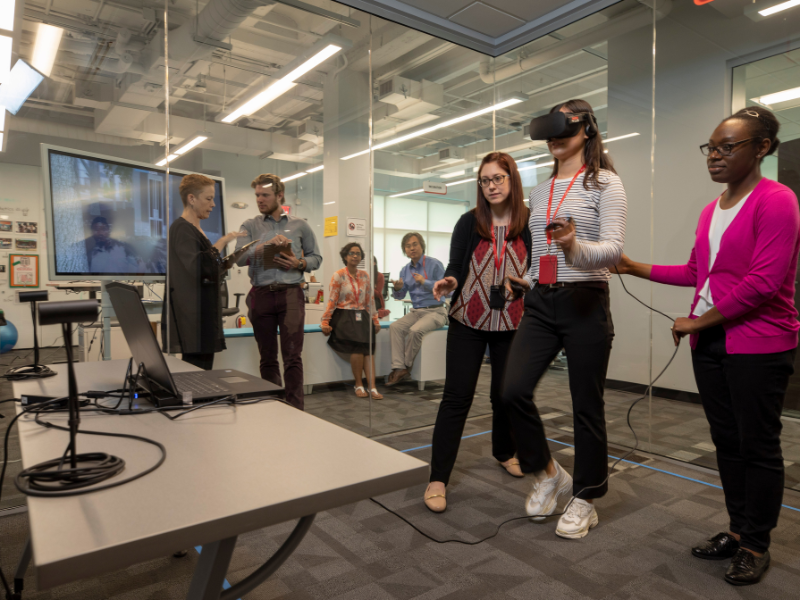 (Front L-R) Graduate students Katie Walters, Yuri Lee and Cheryl Wilson experiment with virtual reality with (Outside L-R) professor Janette Hill, Cory Gleasman, Swagata Das and professor Ikeson (Ike) Choi observing in the Research and Innovation in Learning Laboratory (RAIL).