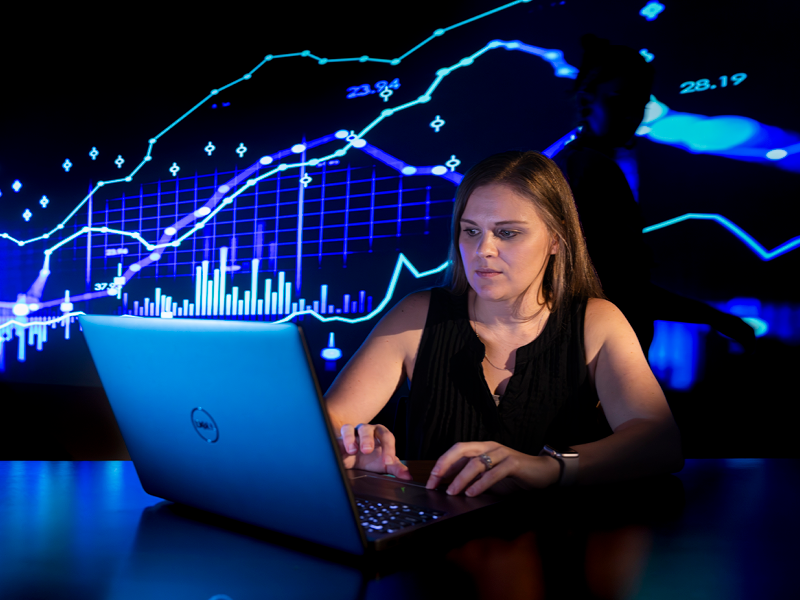 A person working on a laptop computer with graphs and charts projected onto a wall in the background. (UGA)