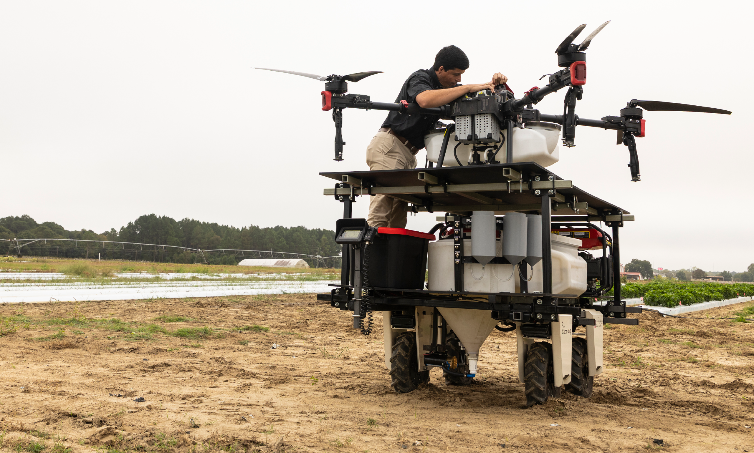 A man working on a large drone in a farm field.